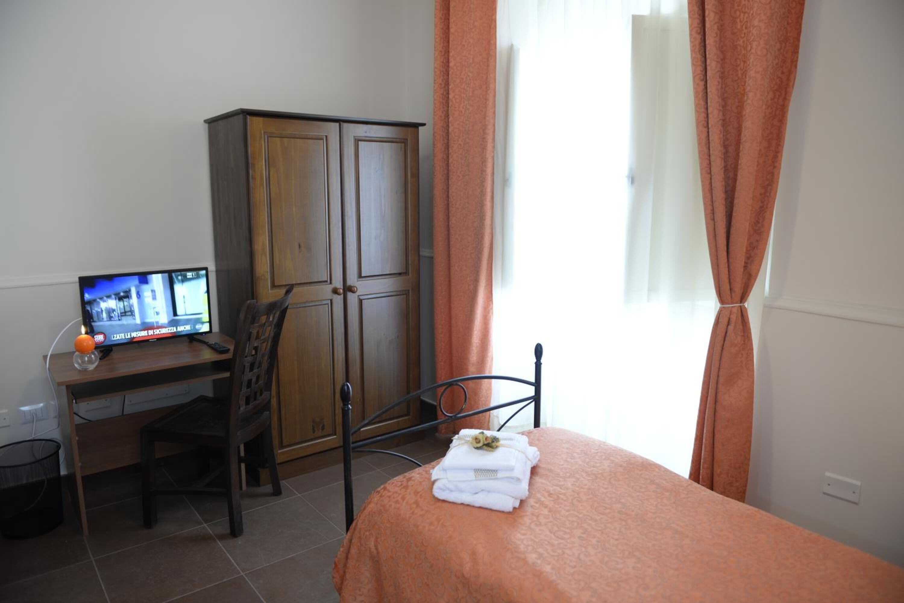 A bedroom with a bed, a desk with a computer, a wardrobe, and a window with curtains.