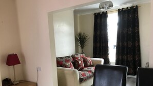 A living room with a sofa, a dining table, and a lamp. - Charming Terrace (Larne)