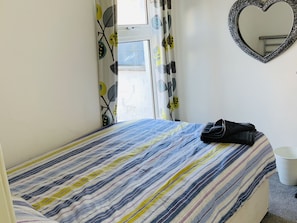 A bed with a striped bedspread, a heart-shaped mirror on the wall, and a window with curtains. - Charming Terrace (Larne)