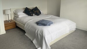 A neatly made bed with white bedding and two patterned pillows, a bedside lamp, and a small wooden nightstand. - Charming Terrace (Larne)