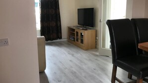 A living room with a wooden entertainment unit, a flat-screen TV, a black leather chair, and a sliding glass door. - Charming Terrace (Larne)