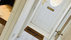 A white door with a glass panel, a doormat with a name, and a wooden floor. - Charming Terrace (Larne)