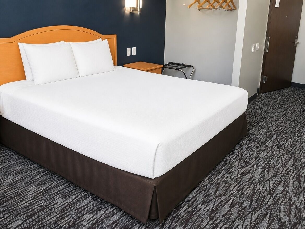 A neatly made bed with a wooden headboard, a small bedside table, and a wall-mounted light fixture.