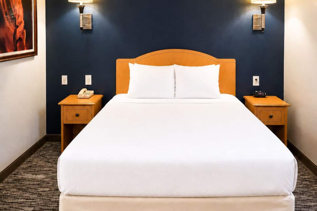 A hotel room with a large bed, two bedside tables with lamps, a telephone, and a painting on the wall.