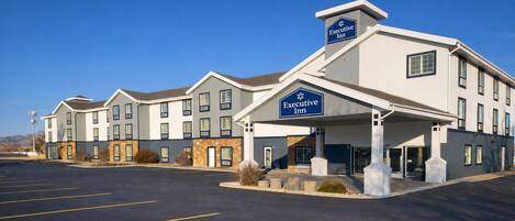 A hotel with a modern design, featuring a central entrance with a sign, multiple windows, and a parking lot.