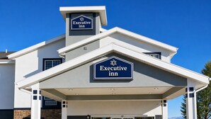 Een hotel met een opvallend bord waarop 'Executive Inn' staat, een overdekte ingang en een aangelegde voortuin met diverse bloemen.