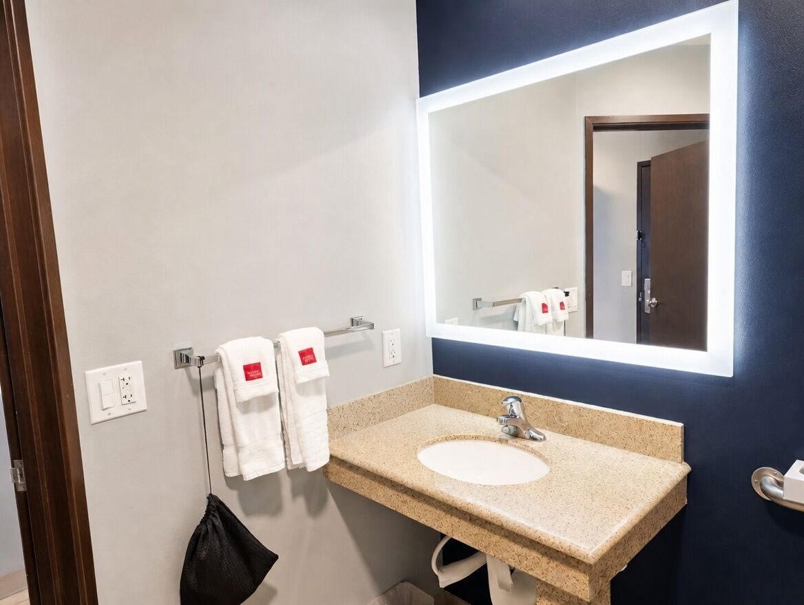 Un baño con lavamanos, espejo, toallas y una puerta.