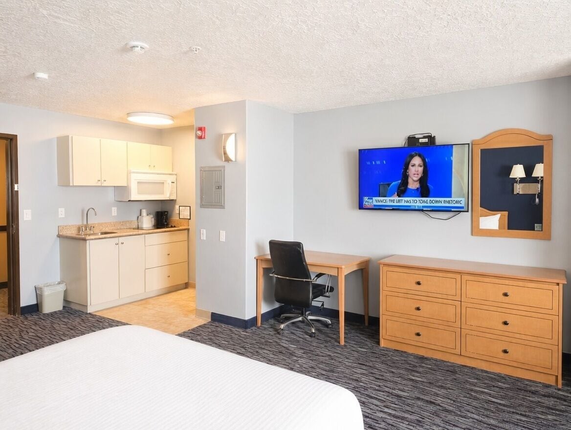 Ein Hotelzimmer mit Bett, Schreibtisch, Stuhl, Fernseher, Mikrowelle, Spüle und Kleiderschrank.