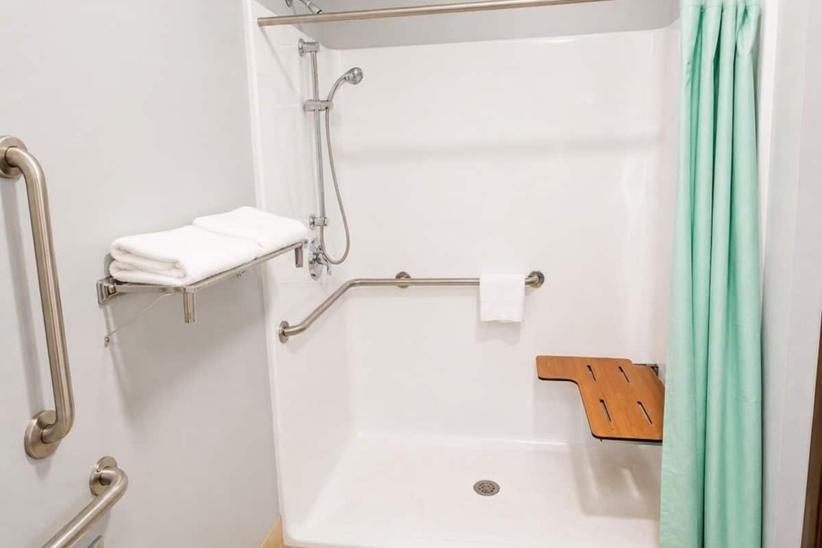 A shower with a grab bar, a white towel, and a green curtain.