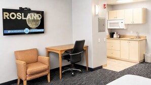 Een kamer met een bureau, een stoel, een bed, een kitchenette en een bord aan de muur.