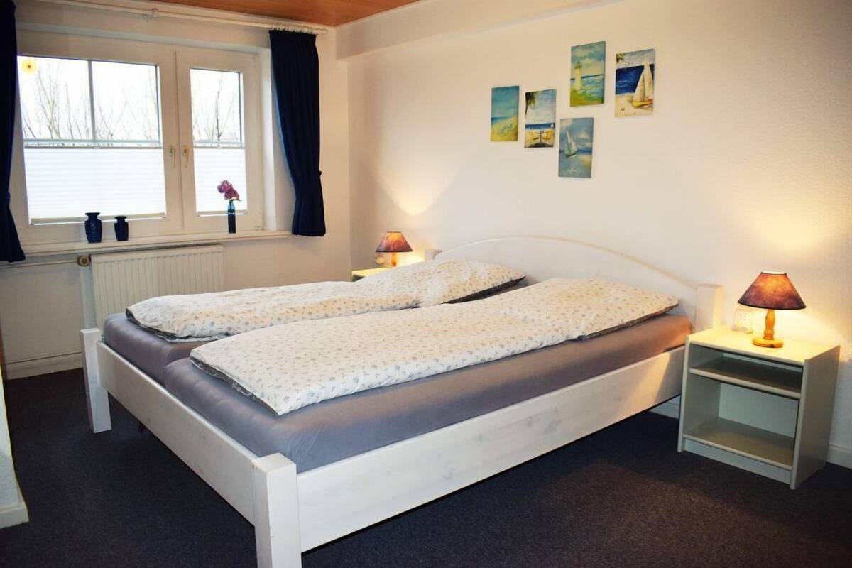 A double bed with two bedside tables, a window with curtains, and a wall with nautical-themed artwork.