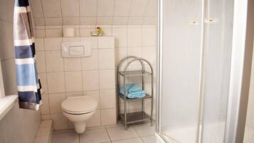 Uma casa de banho com sanita, um porta-toalhas com uma toalha dobrada e uma prateleira com produtos de higiene pessoal.