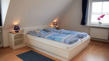 Quarto com cama, duas luminárias de cabeceira, janela com cortinas e radiador.
