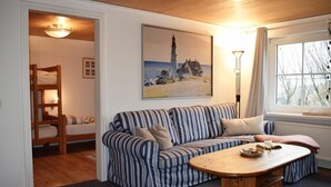 A cozy room with a striped sofa, a wooden table, a bunk bed, and a painting of a lighthouse. - Haus Deichkrone (Dagebuell)