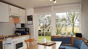 A kitchen with a dining area, including a table and bench, and large windows with a view of the outdoors. - Haus Deichkrone (Dagebuell)
