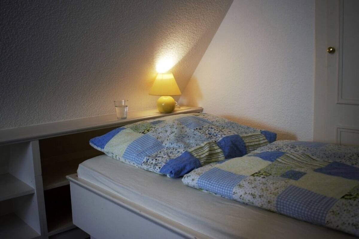 A bedroom with a bed, a nightstand, a lamp, and a door.