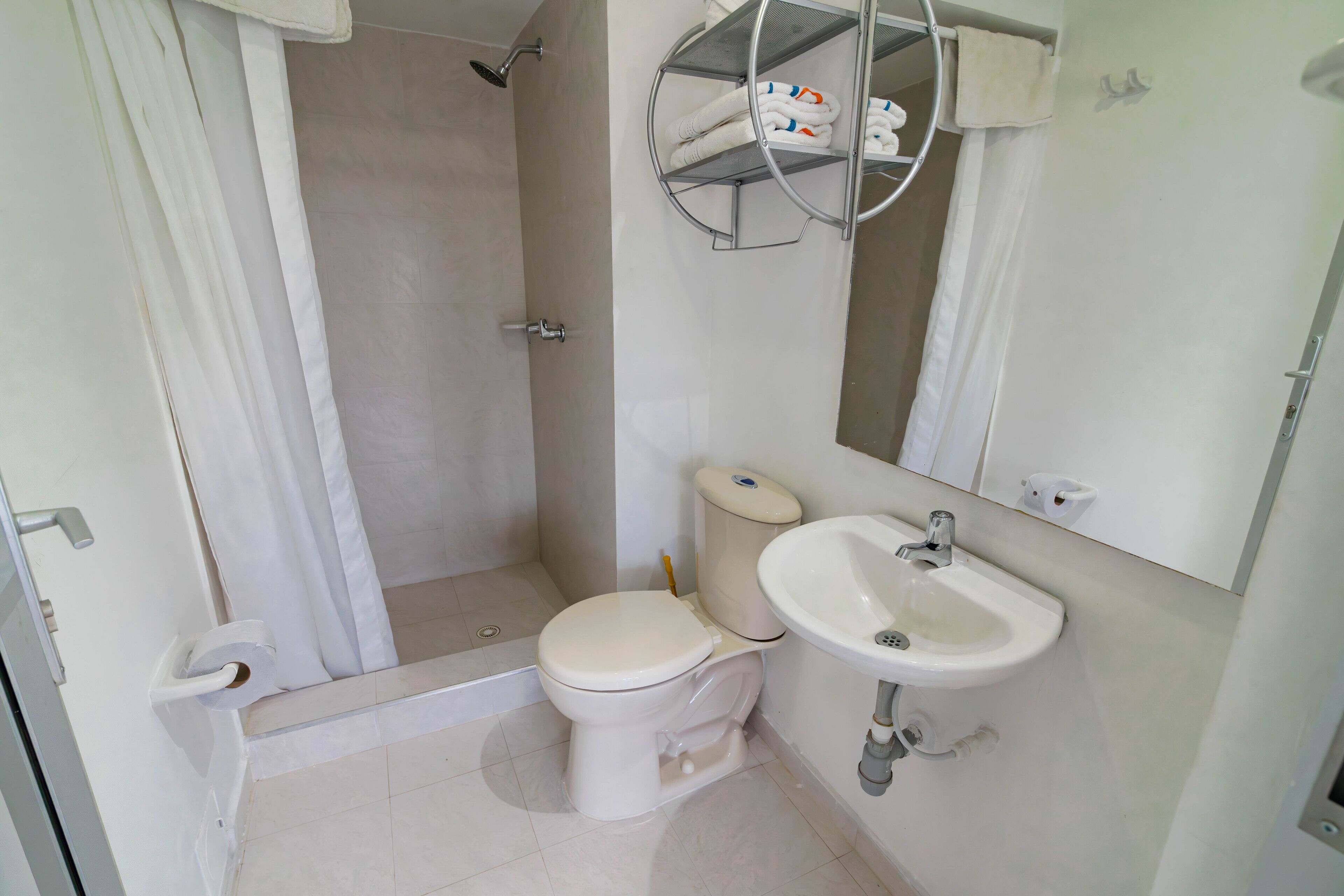 A bathroom with a toilet, sink, shower, and a towel rack with towels.