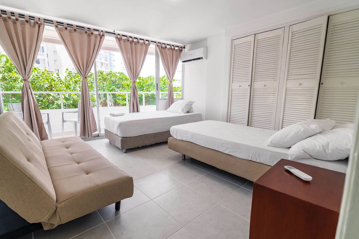 A hotel room with two beds, a sofa, and a balcony with curtains.