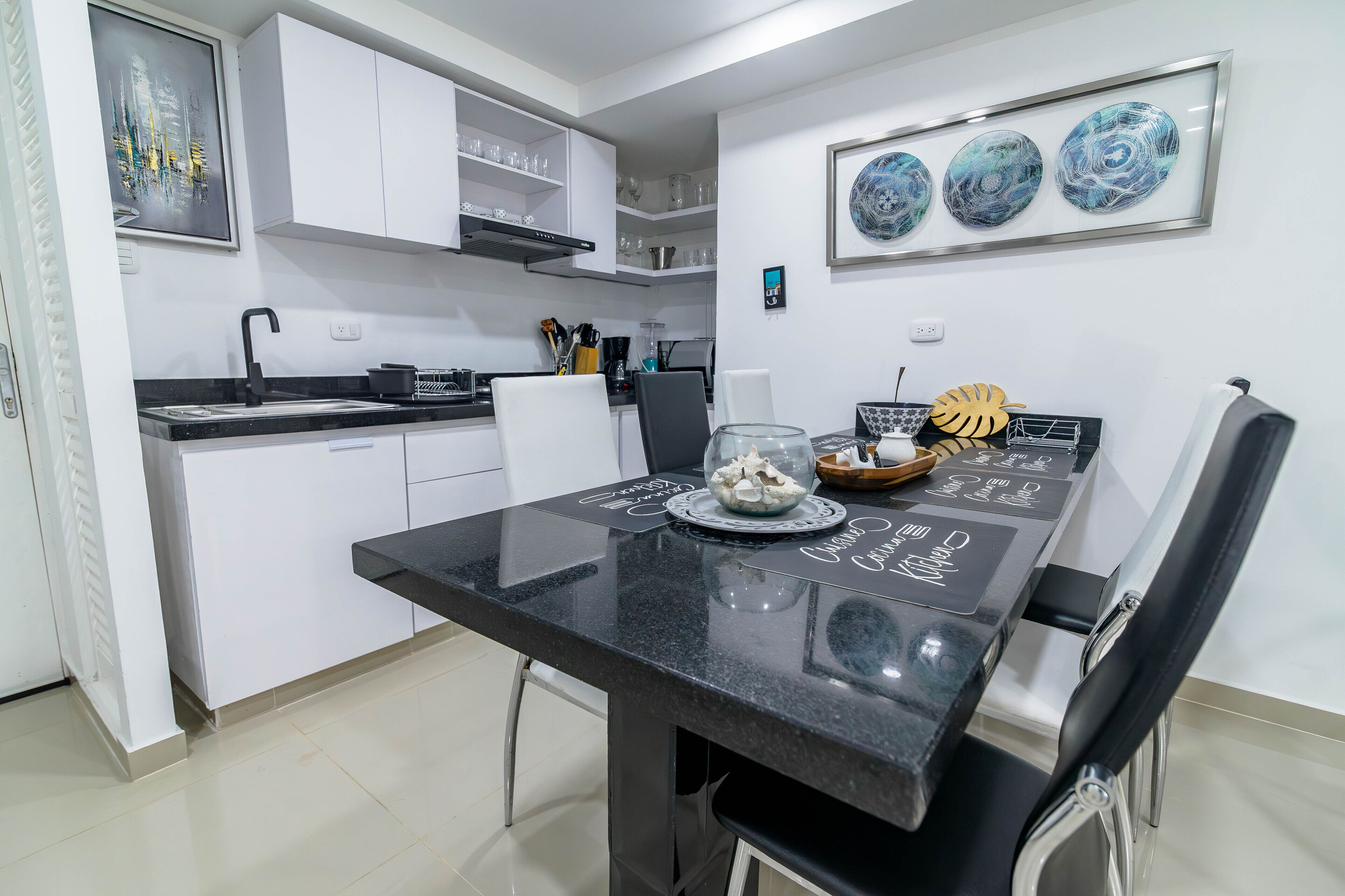 A modern kitchen with white cabinets, a black countertop, and a dining area with a black table and chairs.