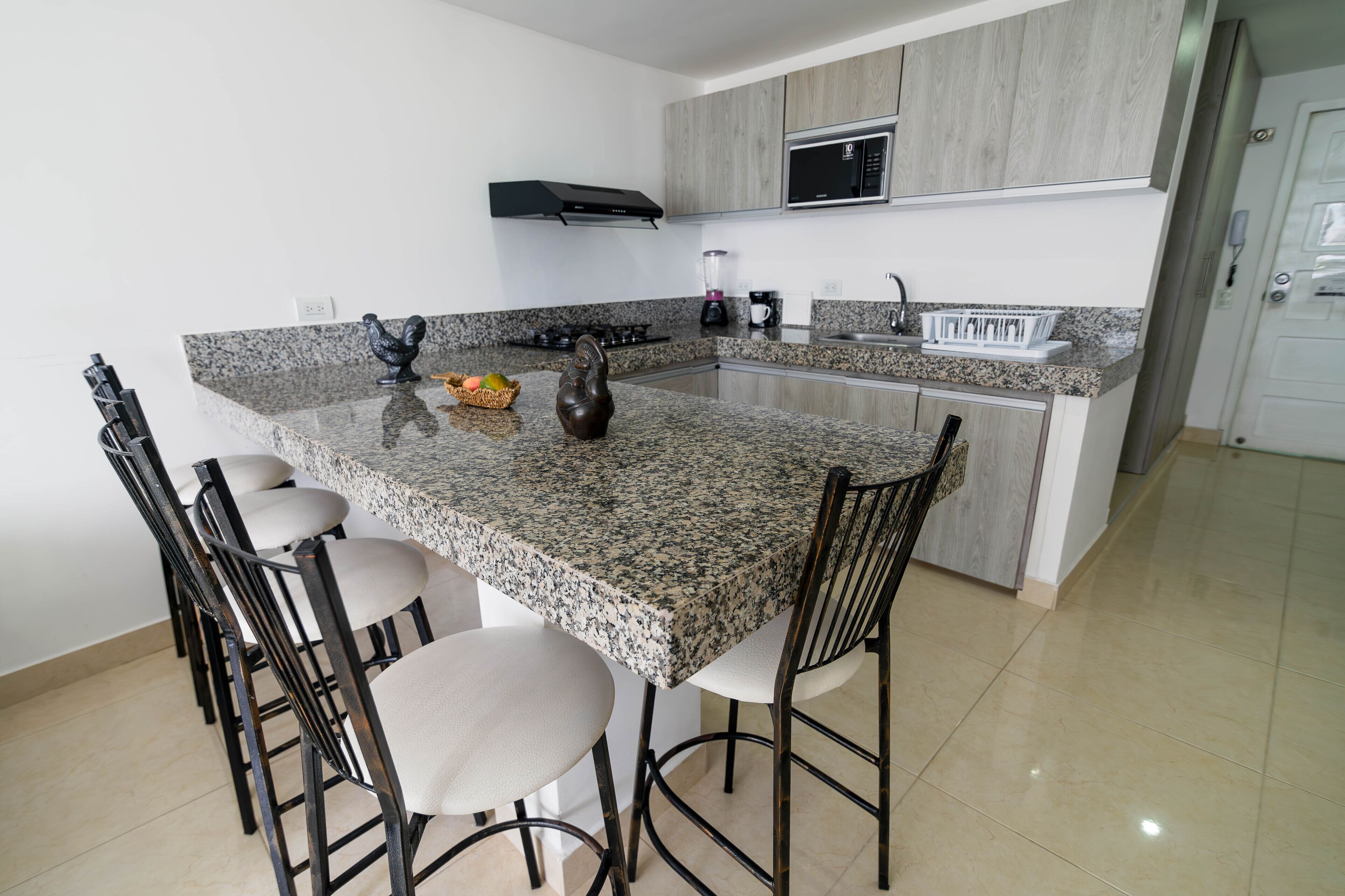 A kitchen with granite countertops, a central island with bar stools, a microwave, and a built-in oven.