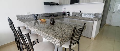 A kitchen with granite countertops, a central island with bar stools, a microwave, and a built-in oven.