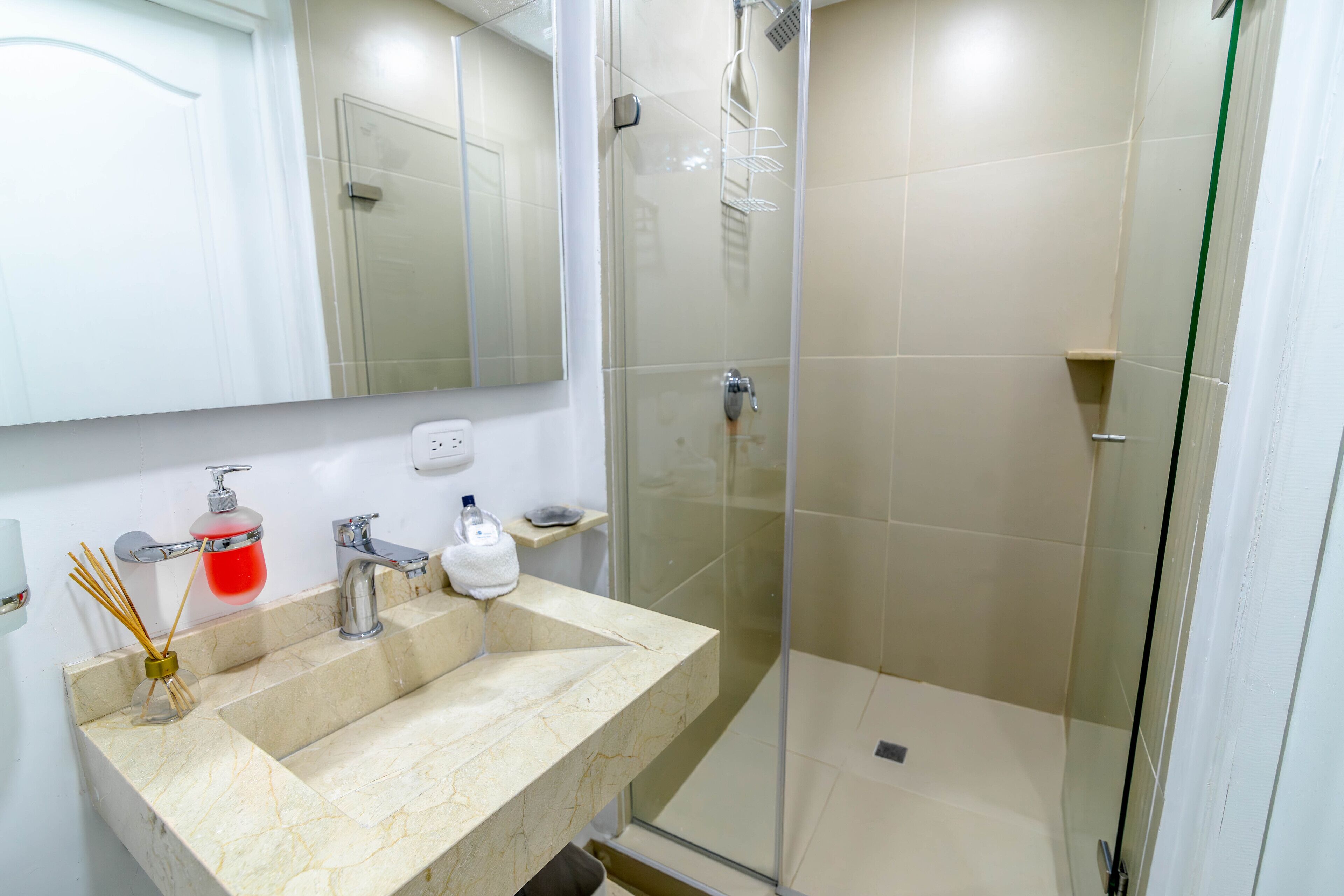 Une salle de bain avec un lavabo en marbre, une cabine de douche en verre et un miroir au-dessus du lavabo.