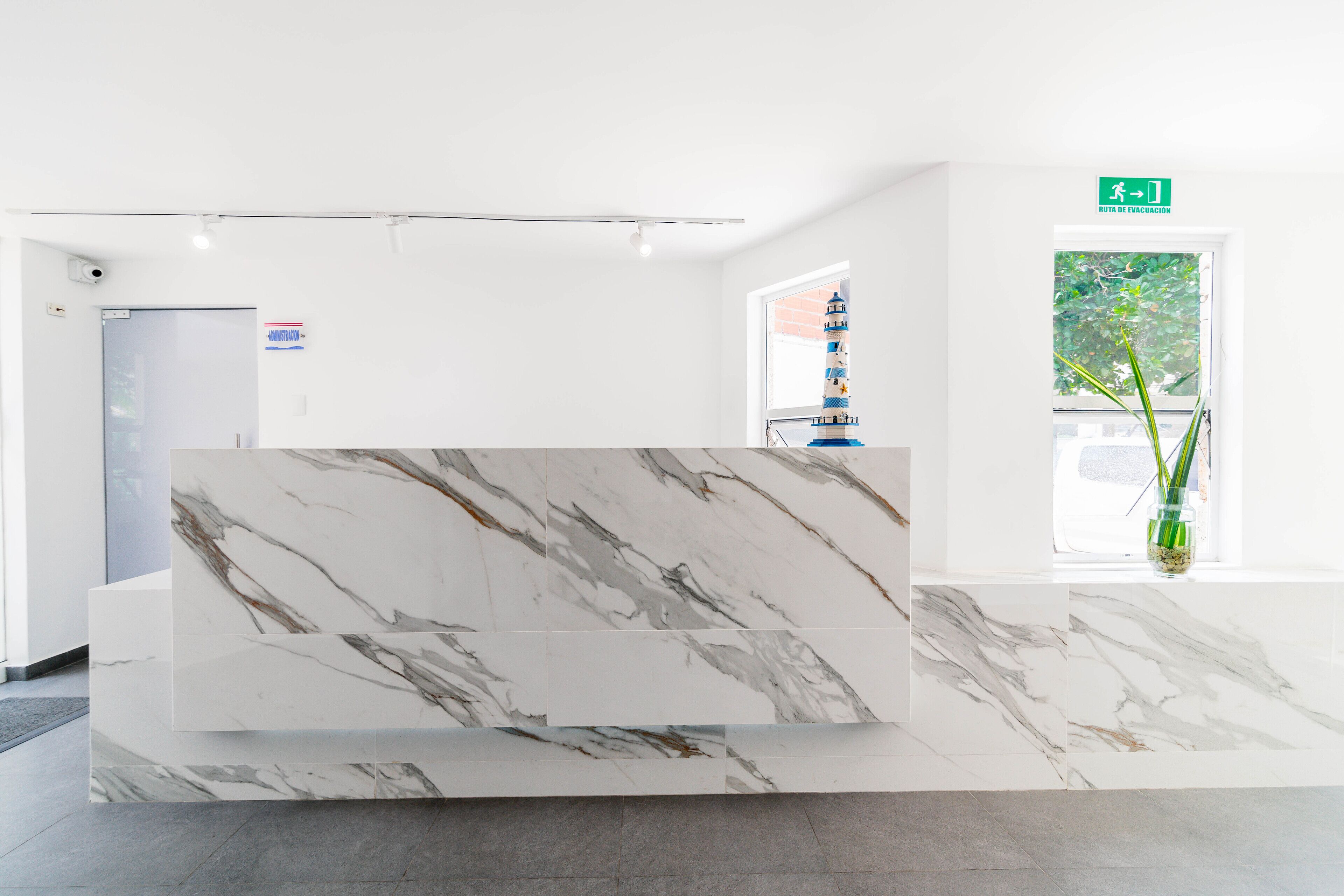 A reception desk with a marble finish, a door with a sign, and a window with a view of greenery.