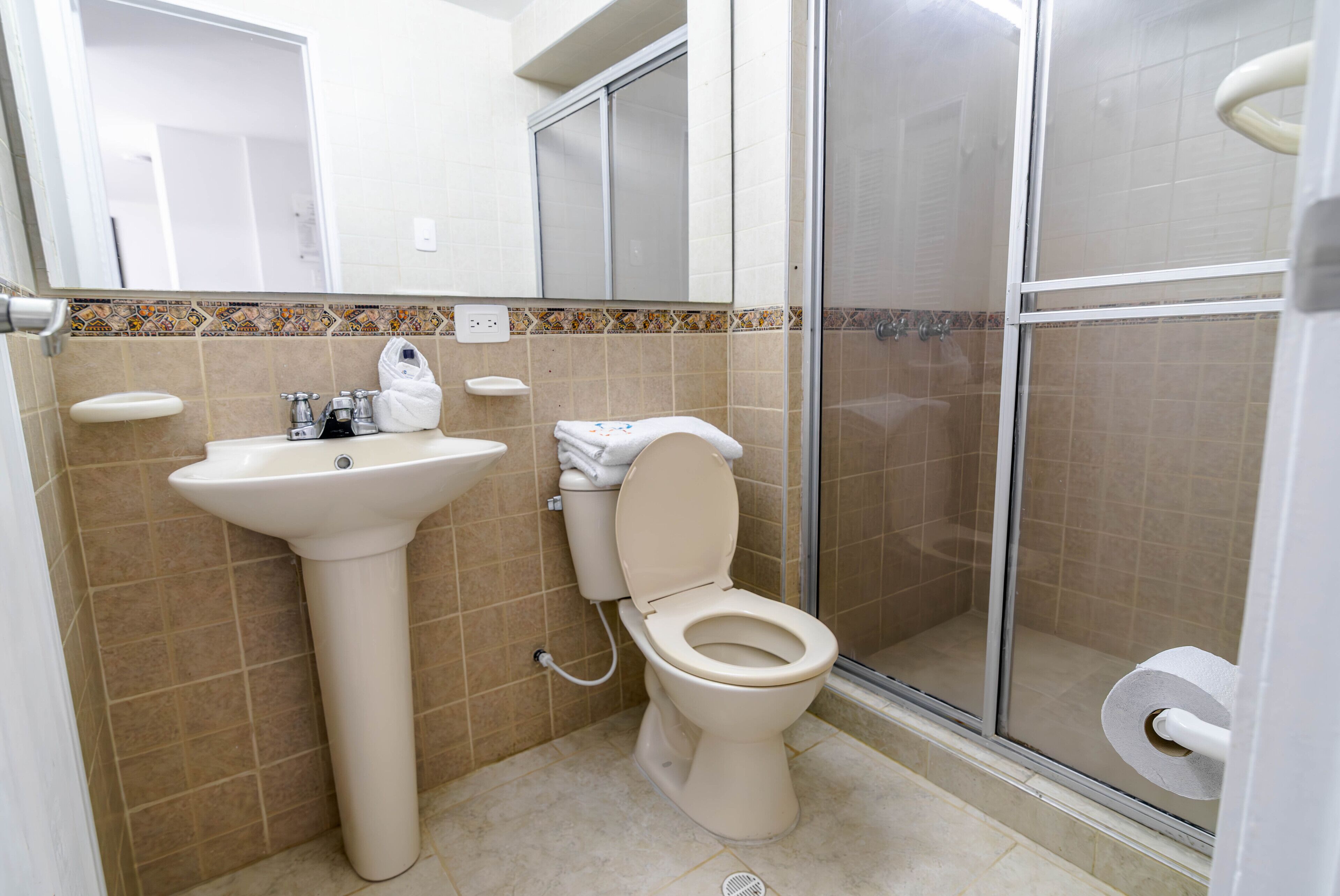 A bathroom with a pedestal sink, toilet, and a glass-enclosed shower stall.