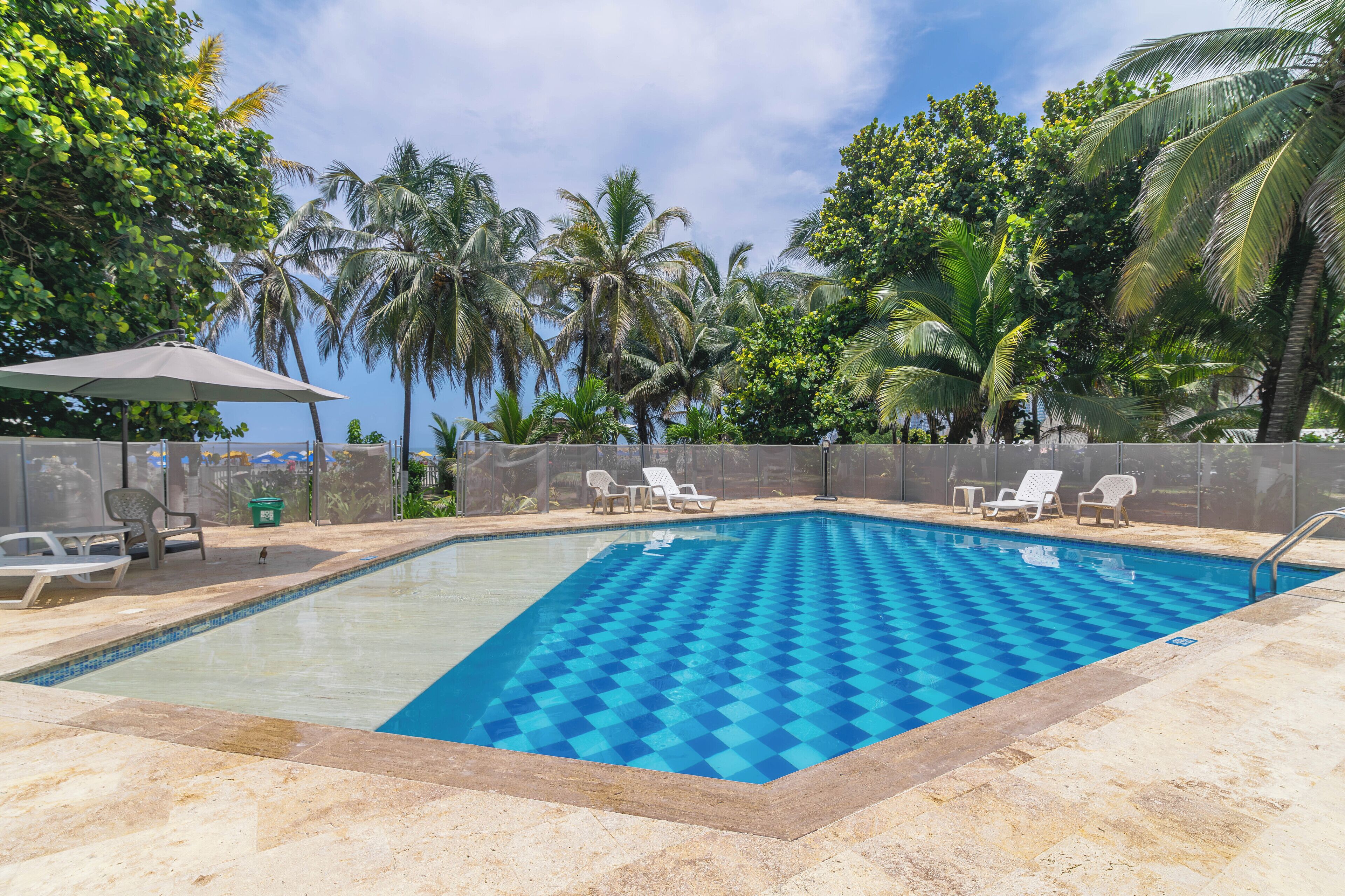 Una piscina con diseño de cuadros, rodeada de palmeras y sillones de descanso.