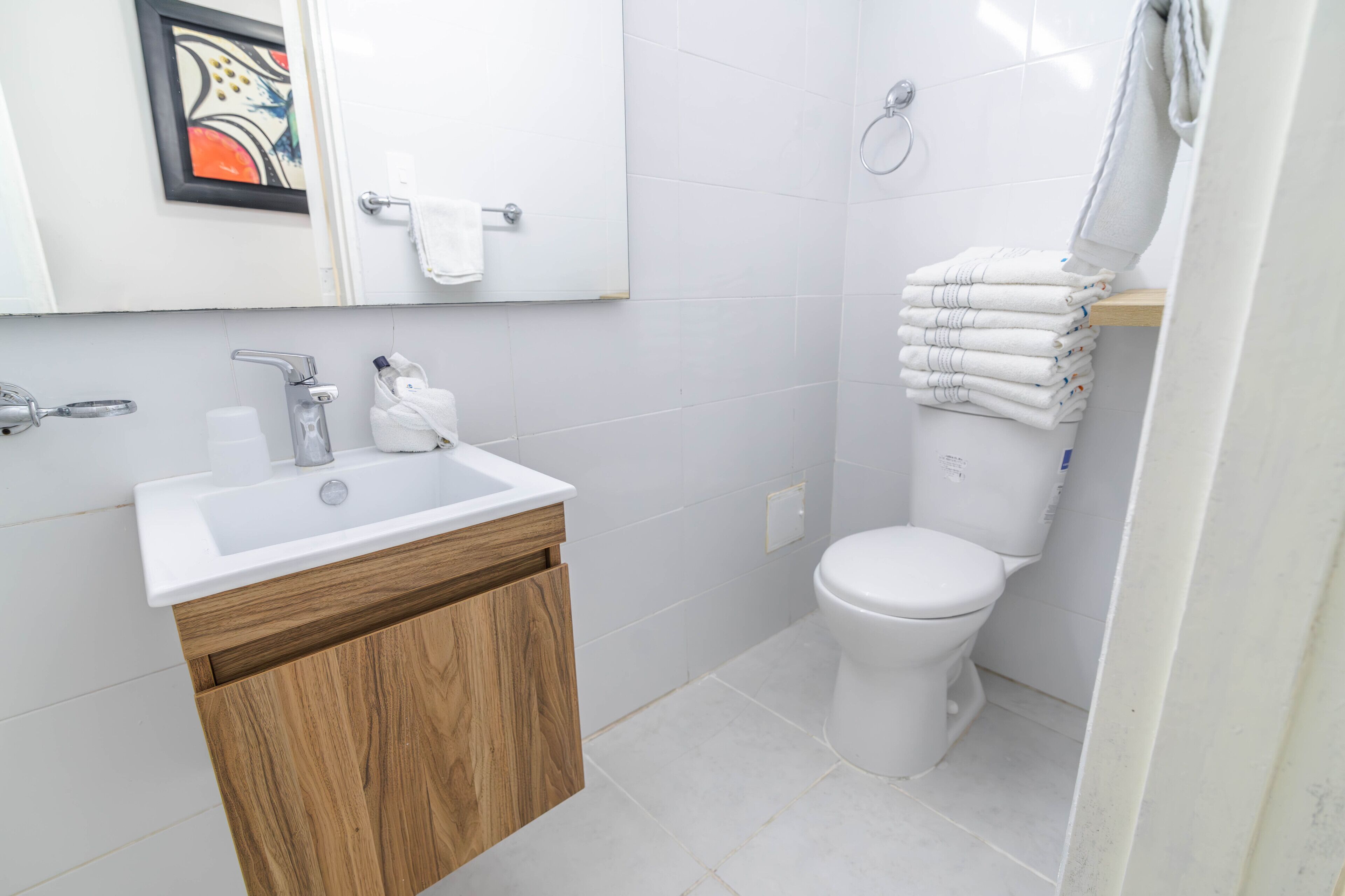 Ein modernes Badezimmer mit einem weißen Waschbecken, einem Holzkabinent, einer weißen Toilette und einem Handtuchhalter mit gefalteten Handtüchern.