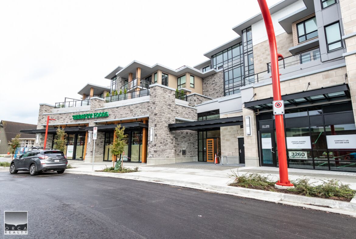 A modern building with a stone facade, a green sign for a restaurant, and a red pole with a no parking sign.