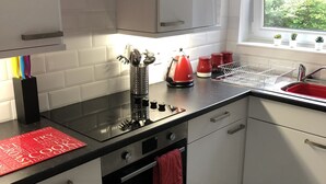Eine moderne Küche mit weißen Schränken, einer schwarzen Arbeitsplatte, einem roten Wasserkocher und einem Fenster mit Pflanzen.
