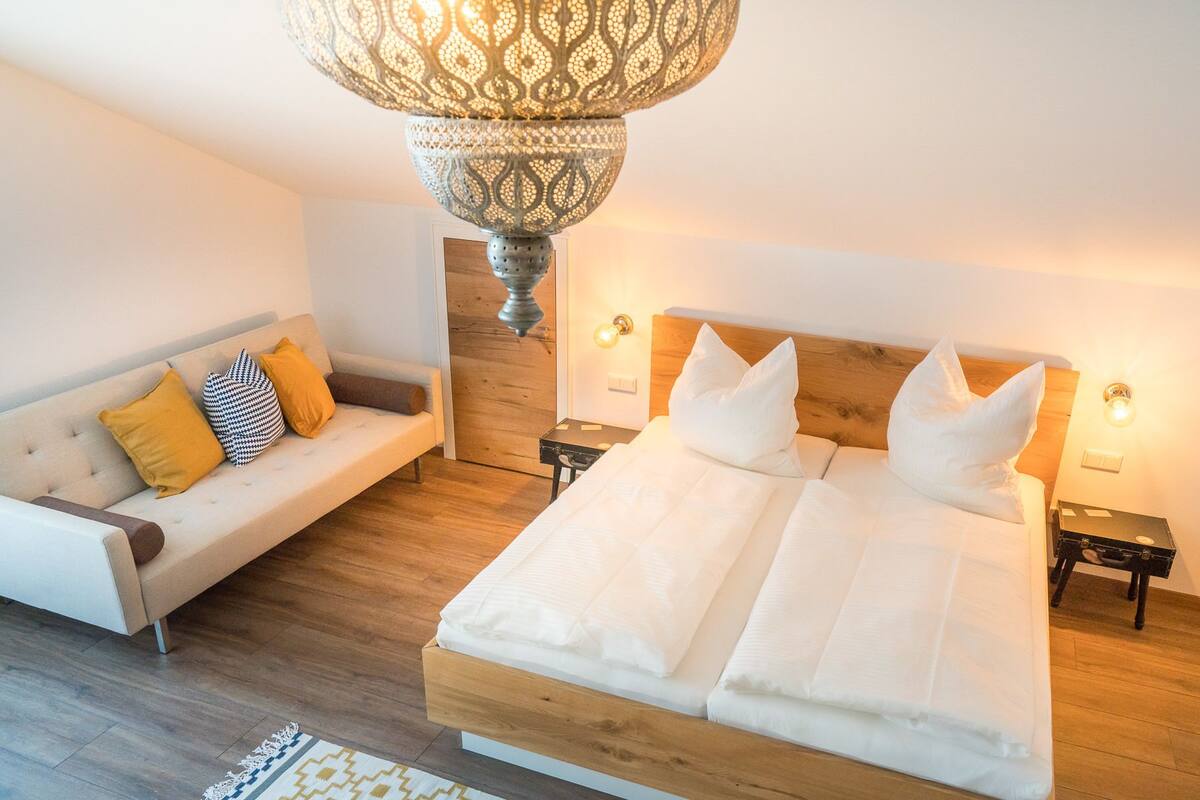 Un dormitorio moderno con una cama grande, un sofá y una lámpara colgante decorativa.