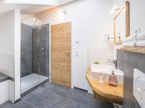 Un baño moderno con ducha envuelta en vidrio, puerta de madera, tocador con lavabo y espejo.