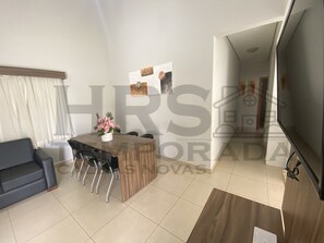 Ein modernes Wohnzimmer mit einem dunklen Sofa, einem Holzespeisetisch mit Stühlen und einem an der Wand montierten Fernseher.
