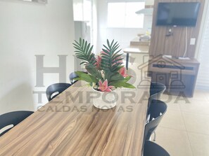 Ein Essbereich mit Holztisch und Stühlen, einer Kübelpflanze mit Blumen und einer Küchenzeile im Hintergrund.