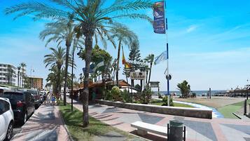 Un paseo marítimo con palmeras, una playa y un restaurante llamado 'Vele'.
