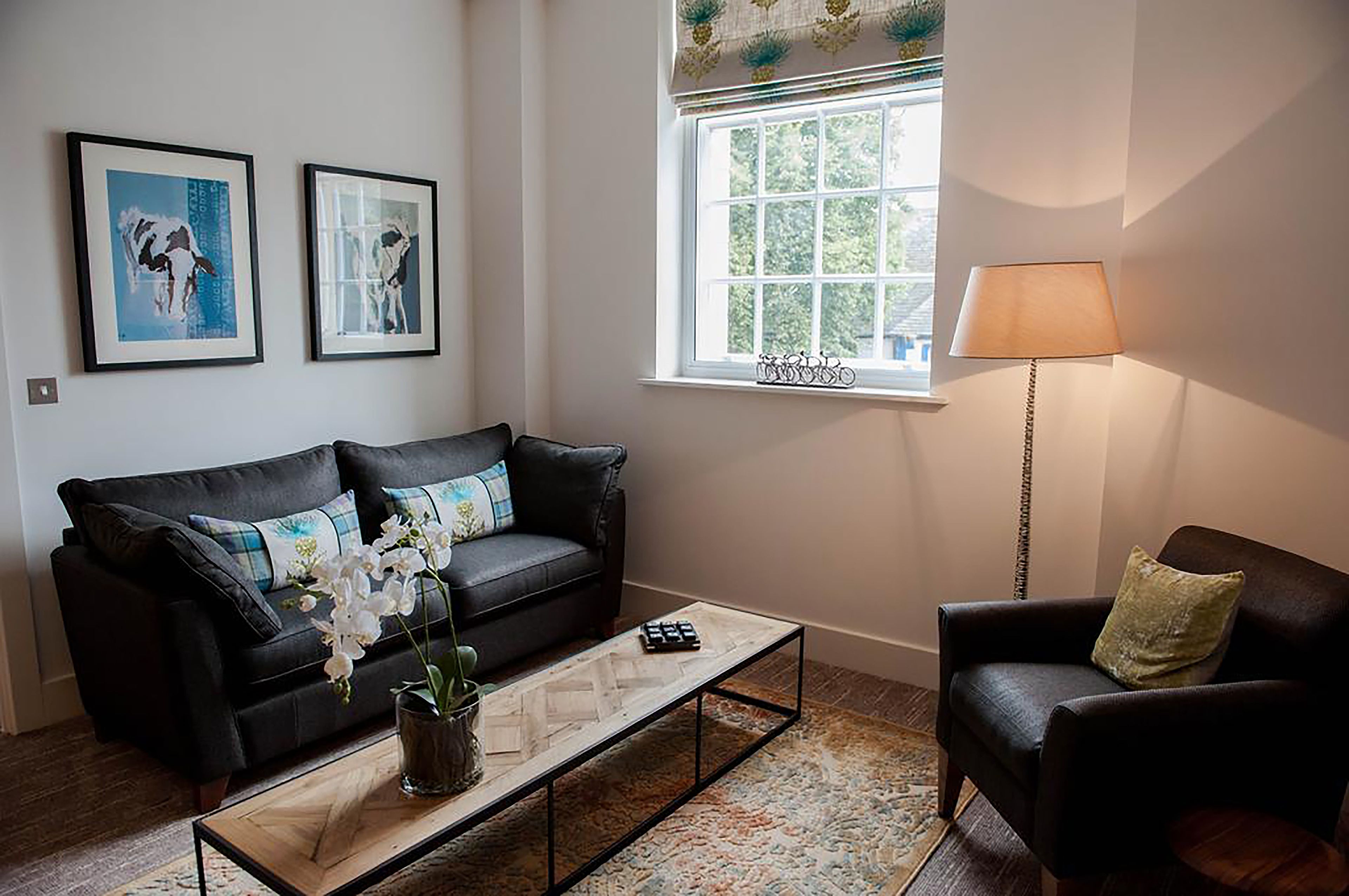 Un salon avec un canapé en cuir noir, une table basse, une table d’appoint, une lampe et deux tableaux encadrés accrochés au mur.