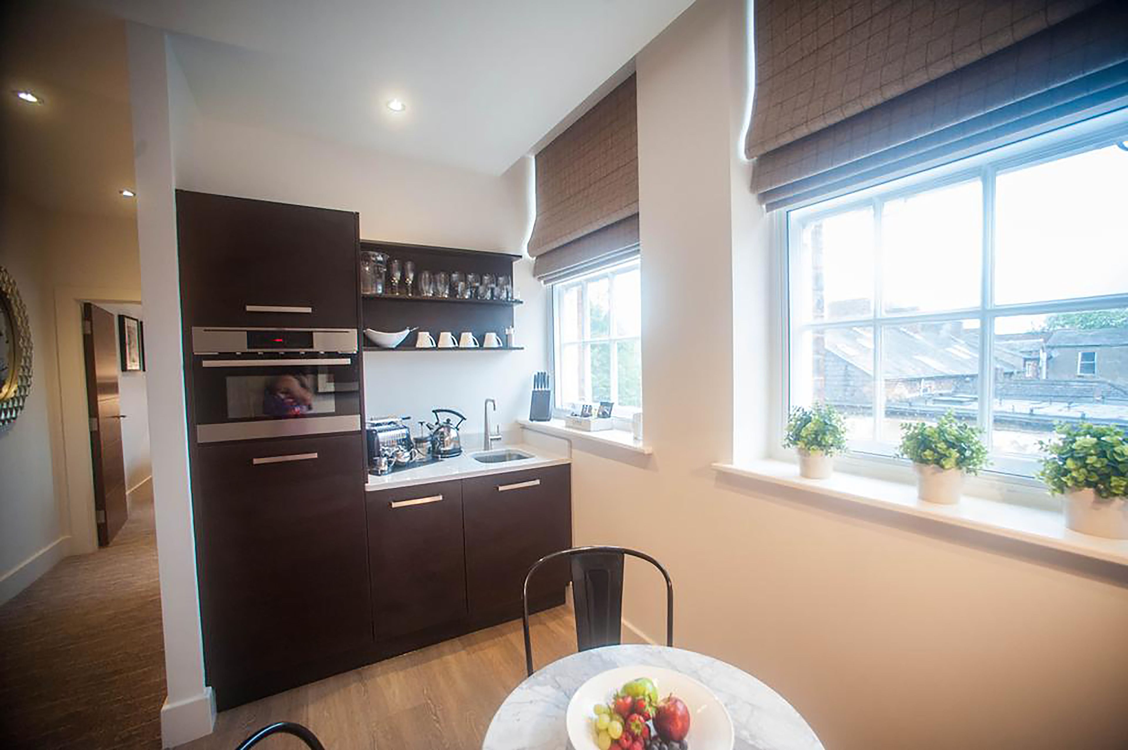 A compact kitchen with dark cabinetry, a built-in oven, and a window with potted plants.