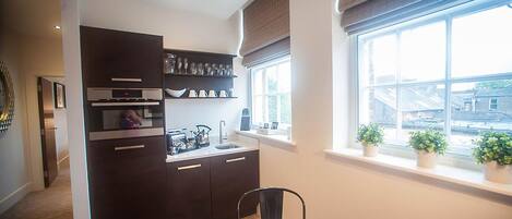 A compact kitchen with dark cabinetry, a built-in oven, and a window with potted plants.