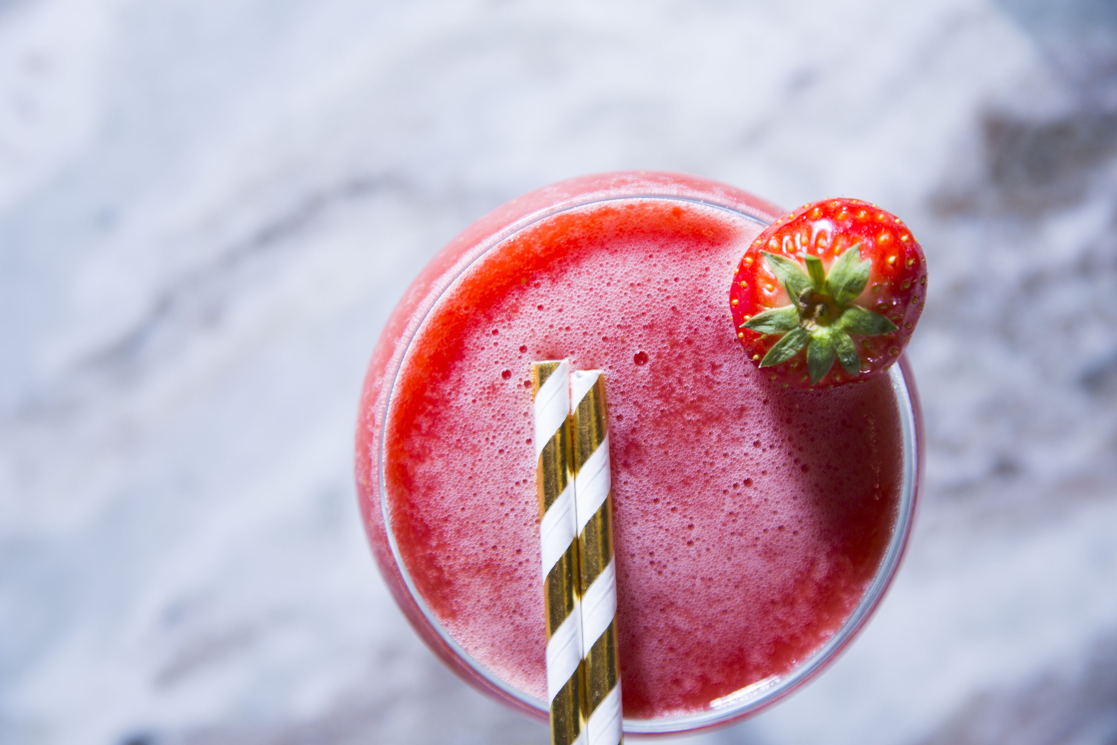 A glass of red beverage with a strawberry garnish and a striped straw.