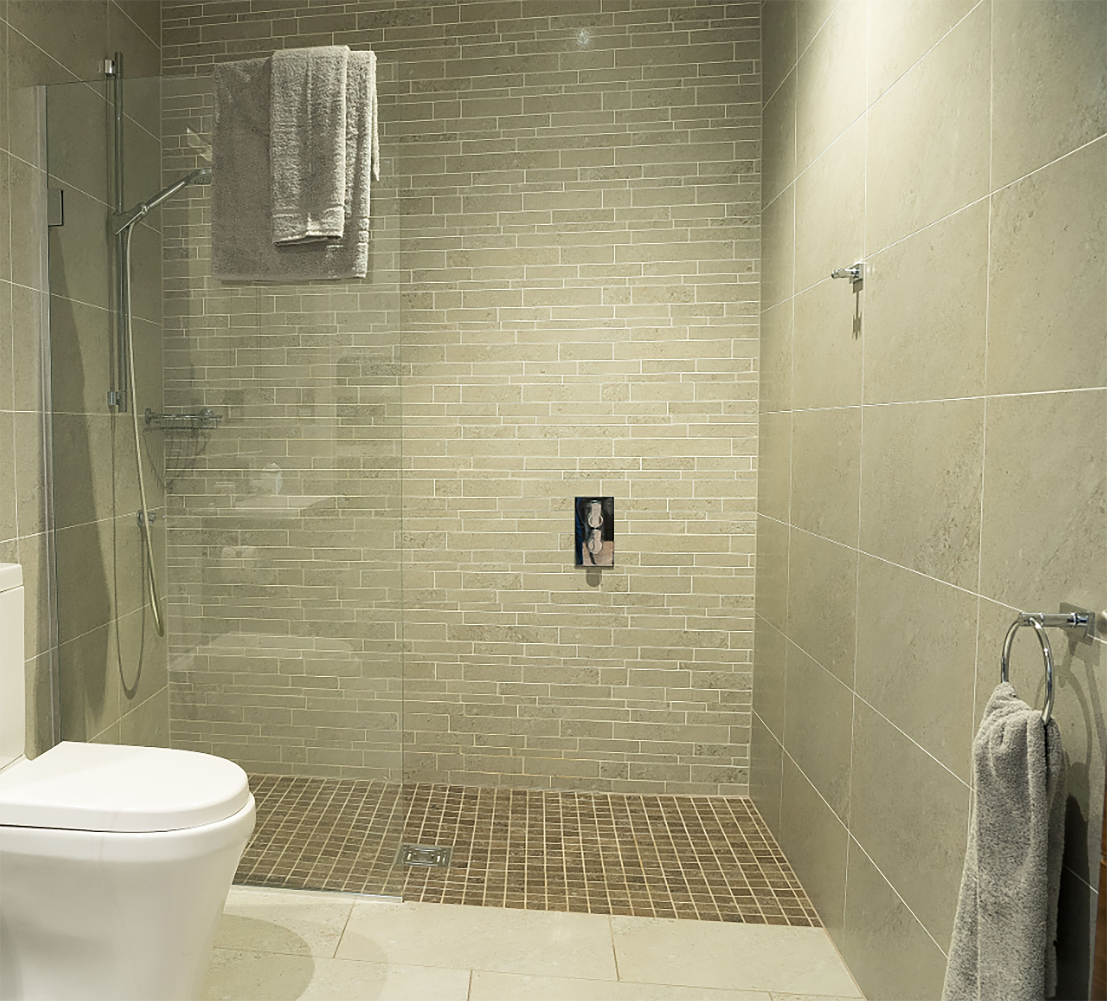 Een moderne badkamer met een douche, toilet en handdoekrek.