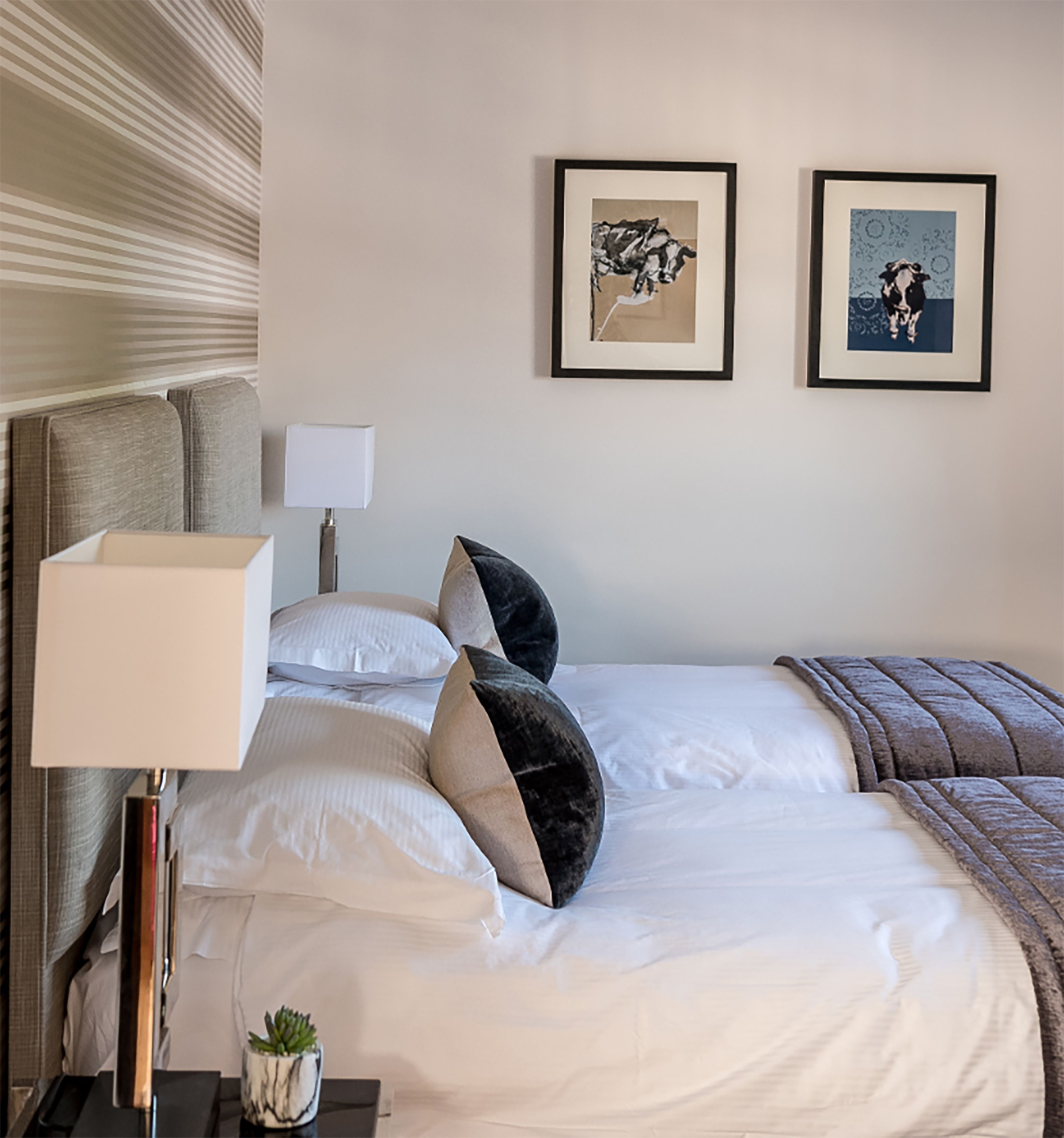 Een hotelkamer met een net opgemaakt bed, een bedlampje, een kleine plant en twee ingelijste foto's aan de muur.