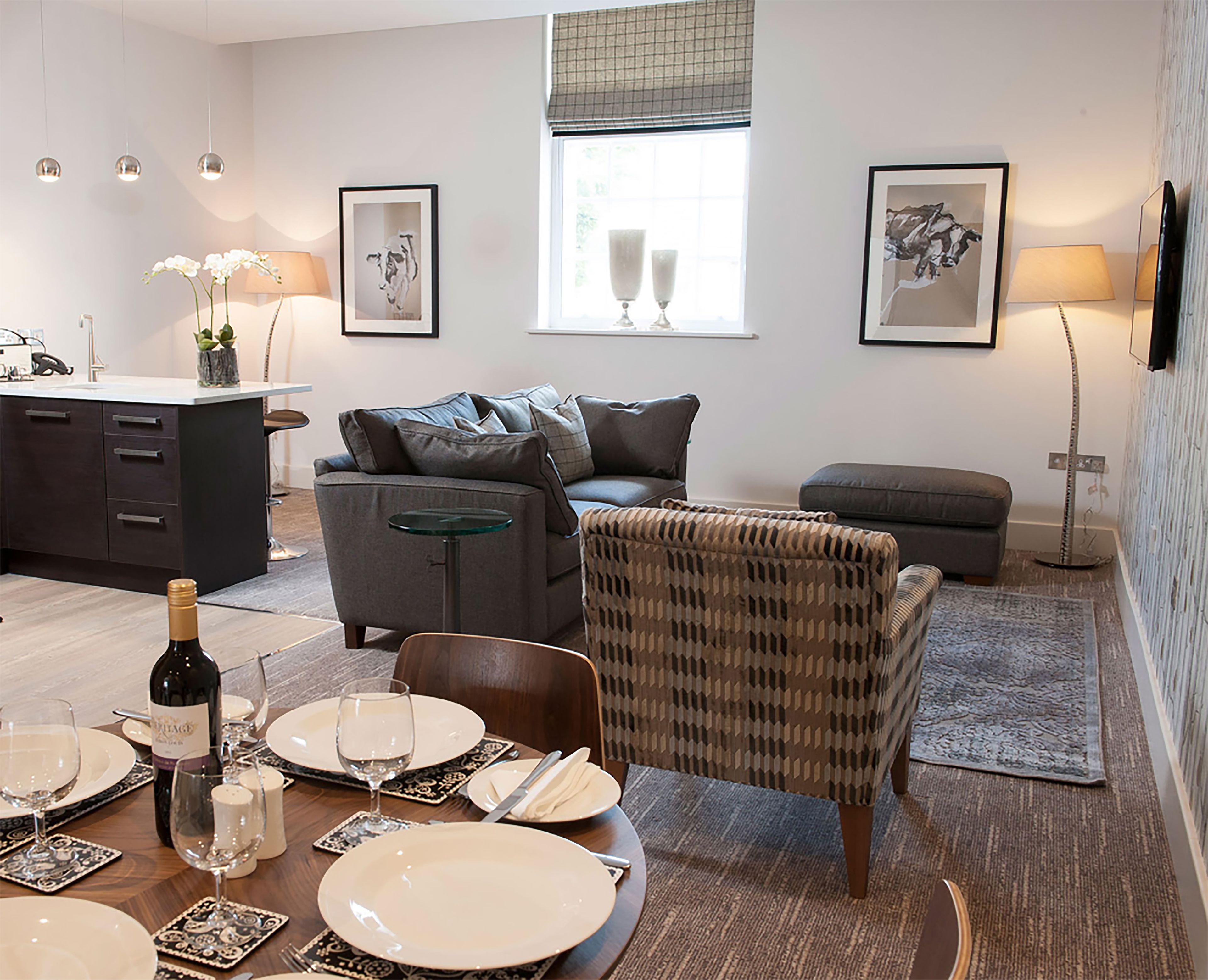 A modern living room with a dining area, grey sofa, armchair, and a small table set for a meal.