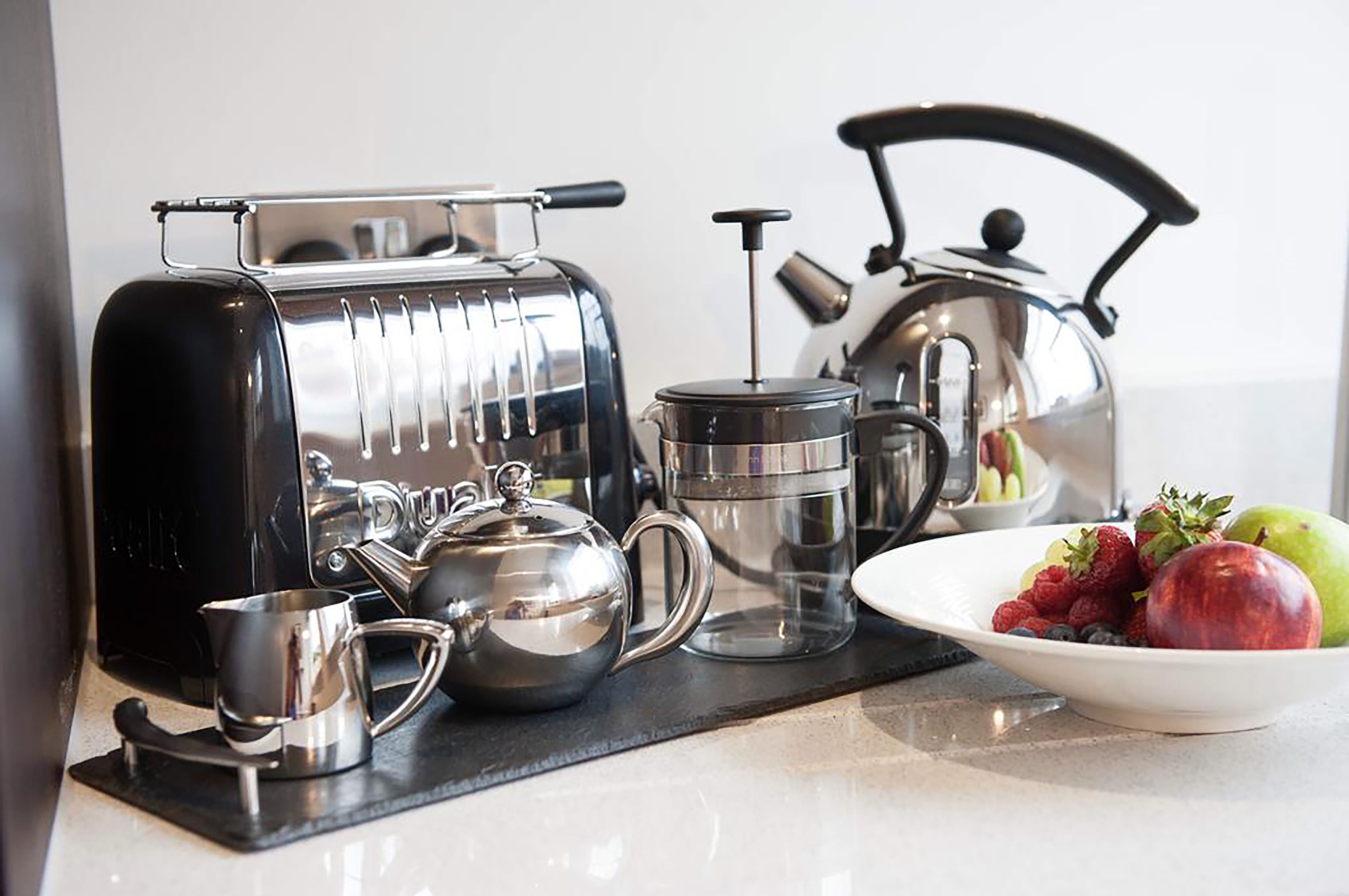 Een keuken met een koffiezetapparaat, waterkoker en een schaal fruit.