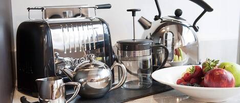 Een keuken met een koffiezetapparaat, waterkoker en een schaal fruit.
