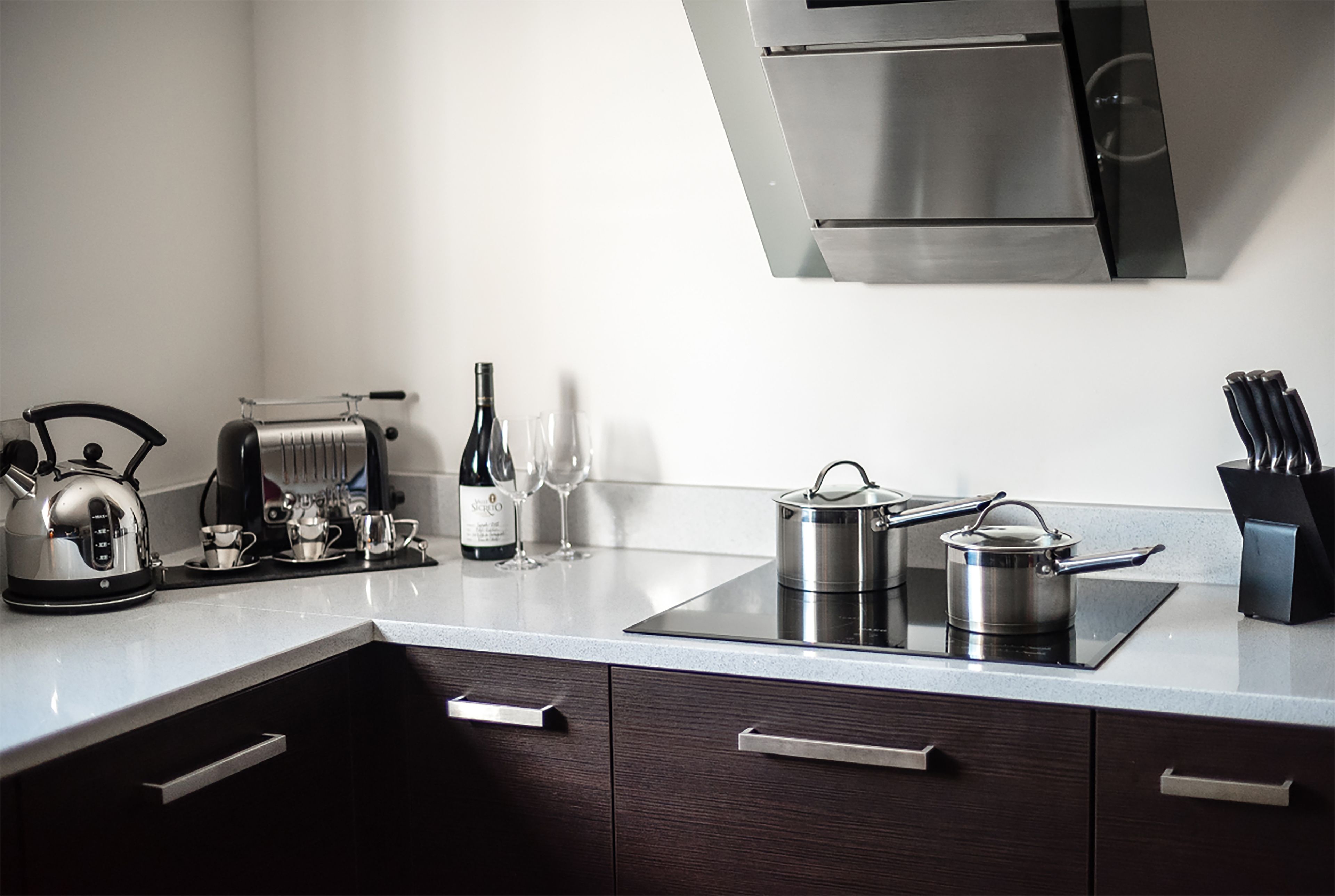 A modern kitchen with a built-in stove, kettle, wine glasses, and a pot on the countertop.