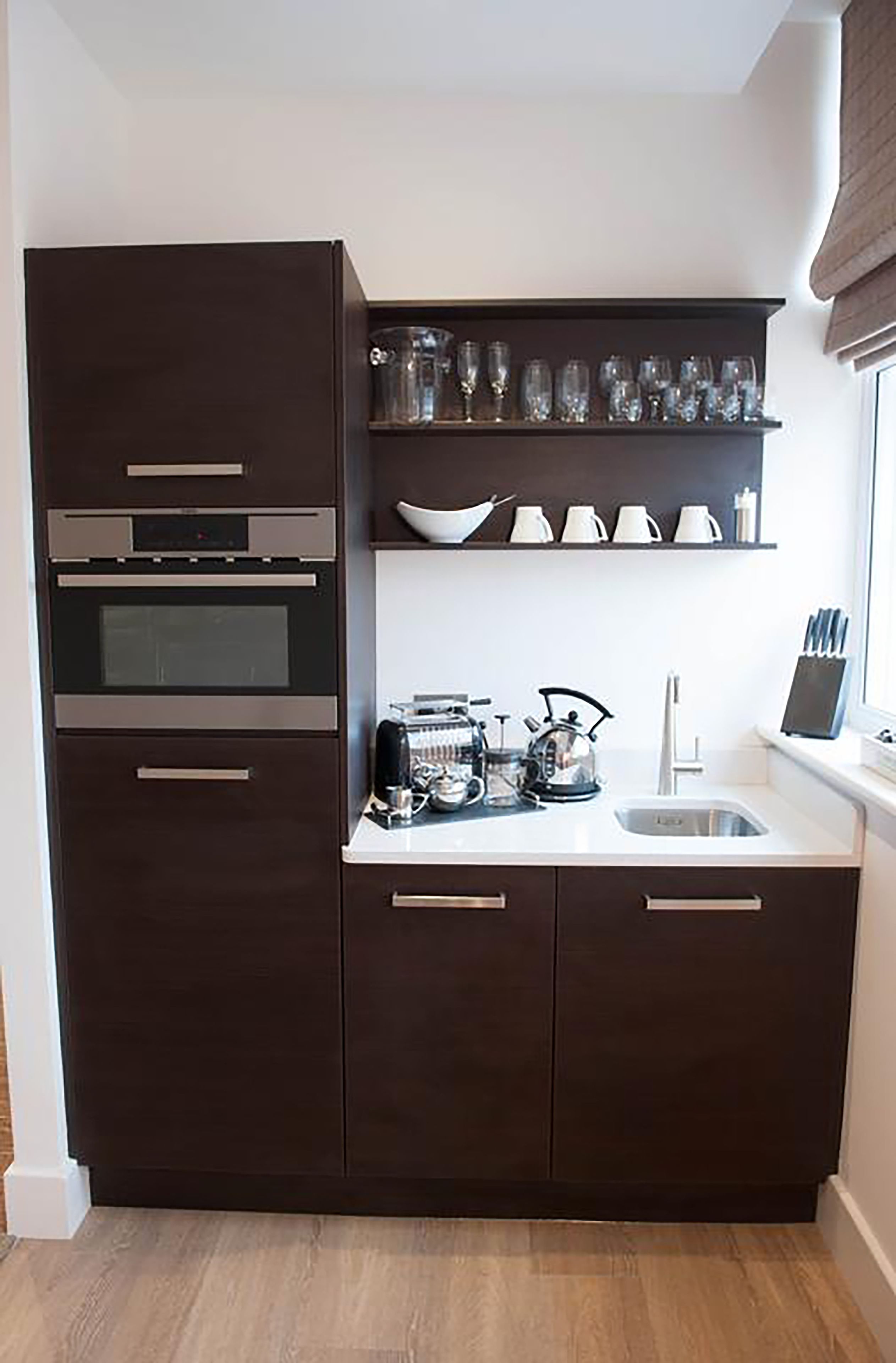 Una cocina compacta con armarios oscuros, horno integrado, pileta y ventana con vista.