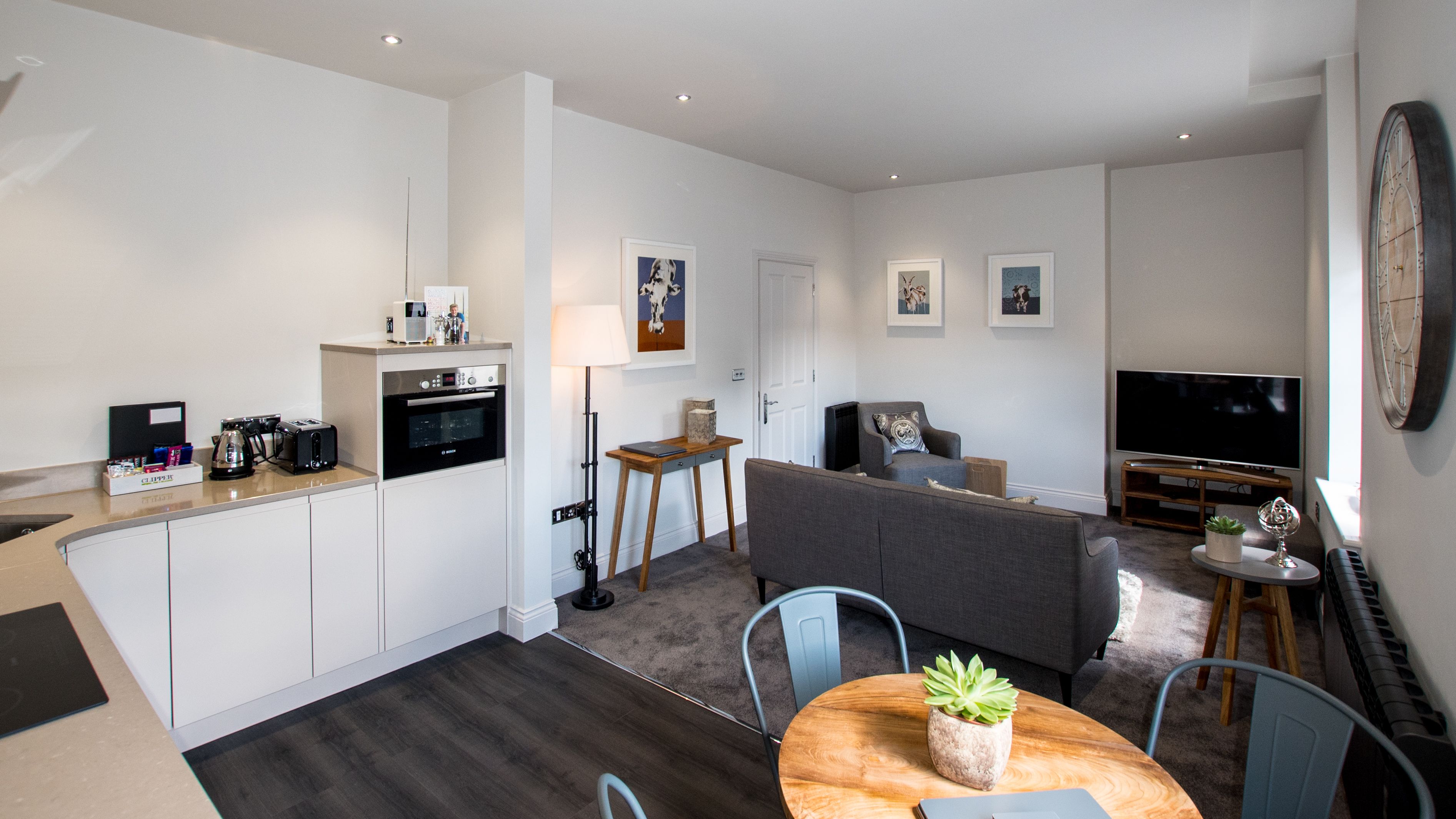 A modern apartment with a kitchen, living area, and dining space. It includes a sofa, a dining table with chairs, a TV, and a piano.