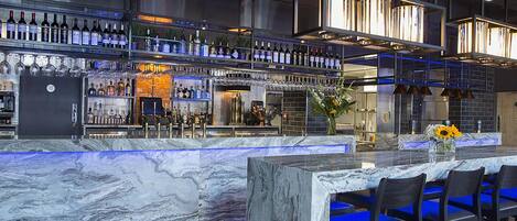 A bar area with a marble countertop, multiple bar stools, and a variety of bottles and glasses on shelves.